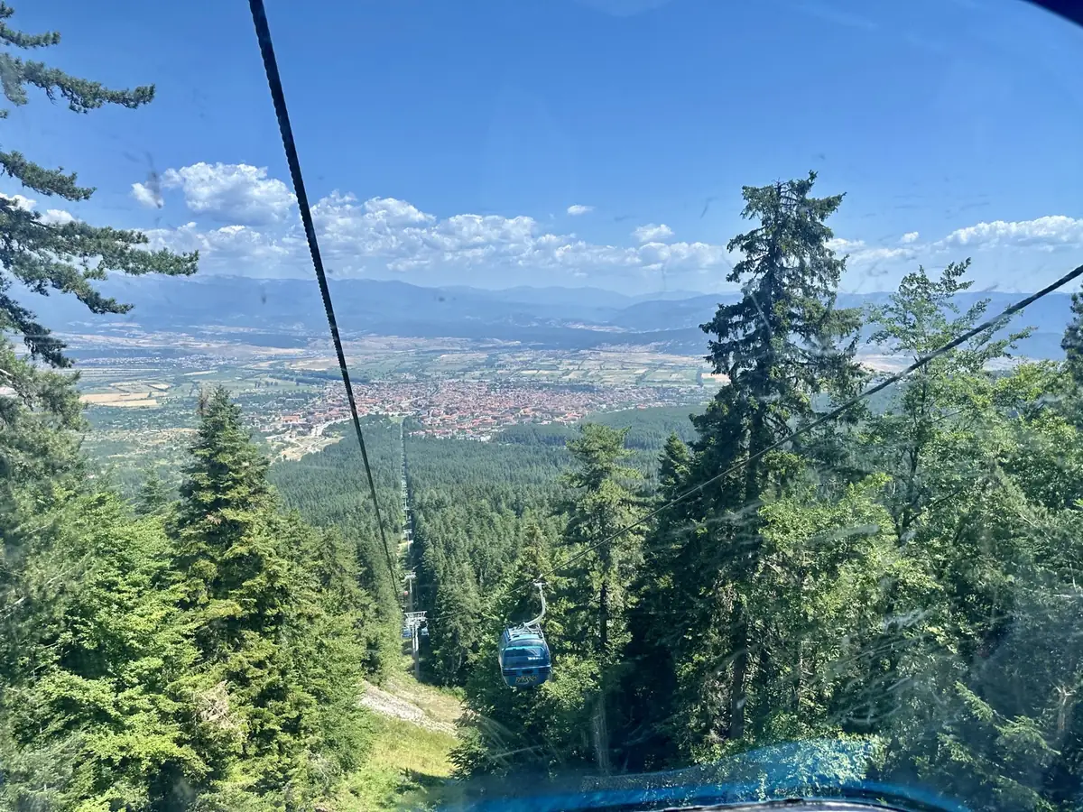 View from inside the Bansko gondola descending over green pine forest towards the town and the valley