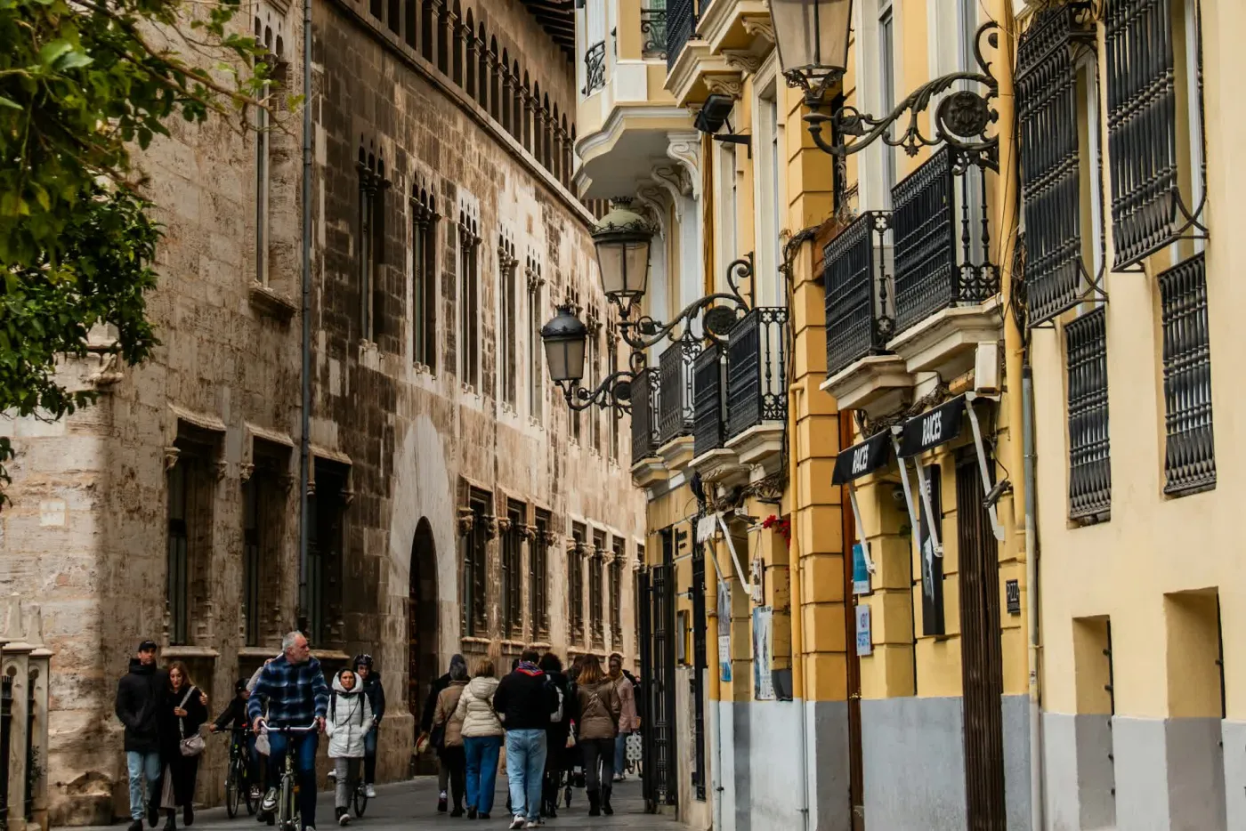 A street in central Valencia, with people walking and cycling past the Gothic stonework of La Lonja and ochre balconied apartment buildings